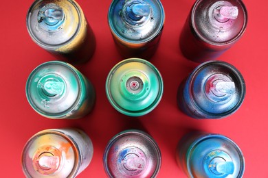 Many spray paint cans on red background, flat lay