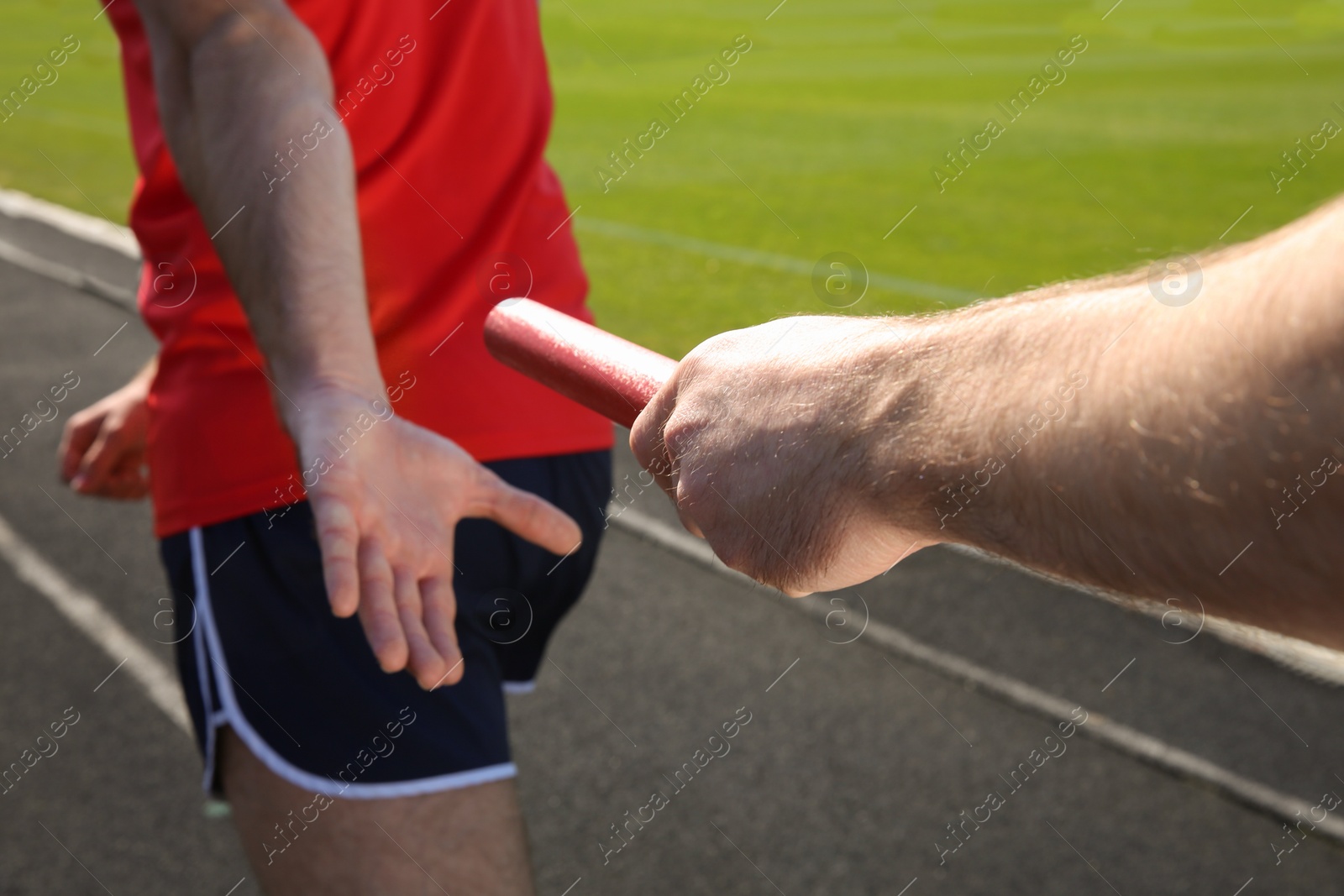 Photo of Man passing baton to his partner at stadium, closeup