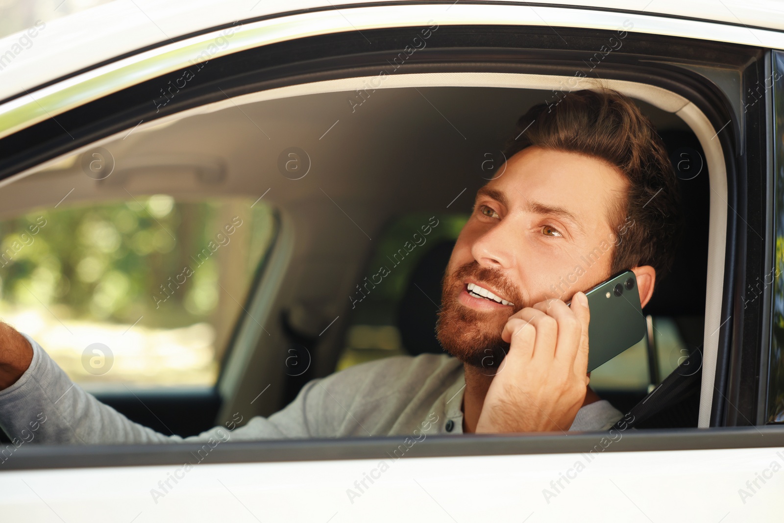 Photo of Happy bearded man talking on smartphone in car, view from outside