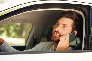 Photo of Happy bearded man talking on smartphone in car, view from outside