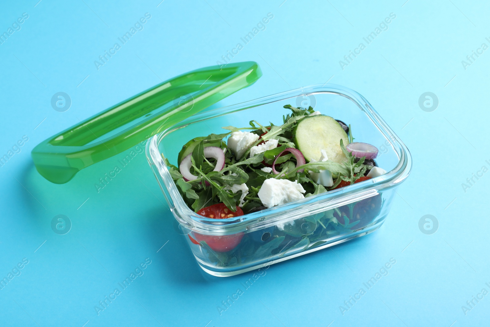 Photo of Tasty salad in glass container on light blue background