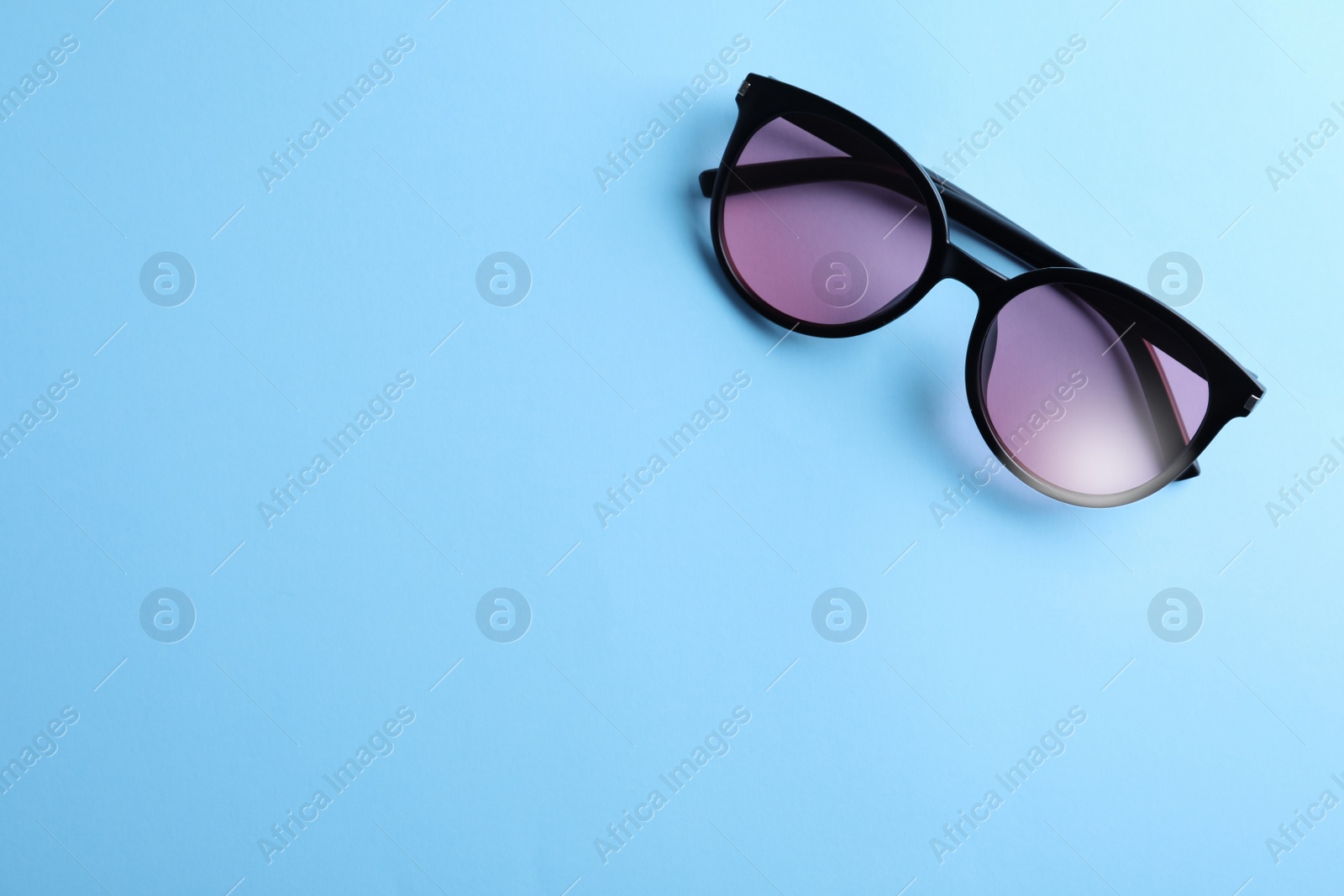 Photo of Stylish sunglasses on light blue background, top view. Space for text