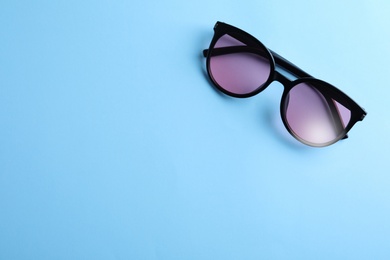 Stylish sunglasses on light blue background, top view. Space for text