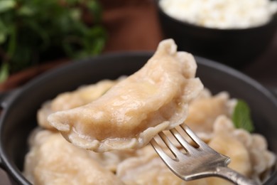 Photo of Delicious dumpling (varenyk) with cottage cheese on fork over bowl, closeup