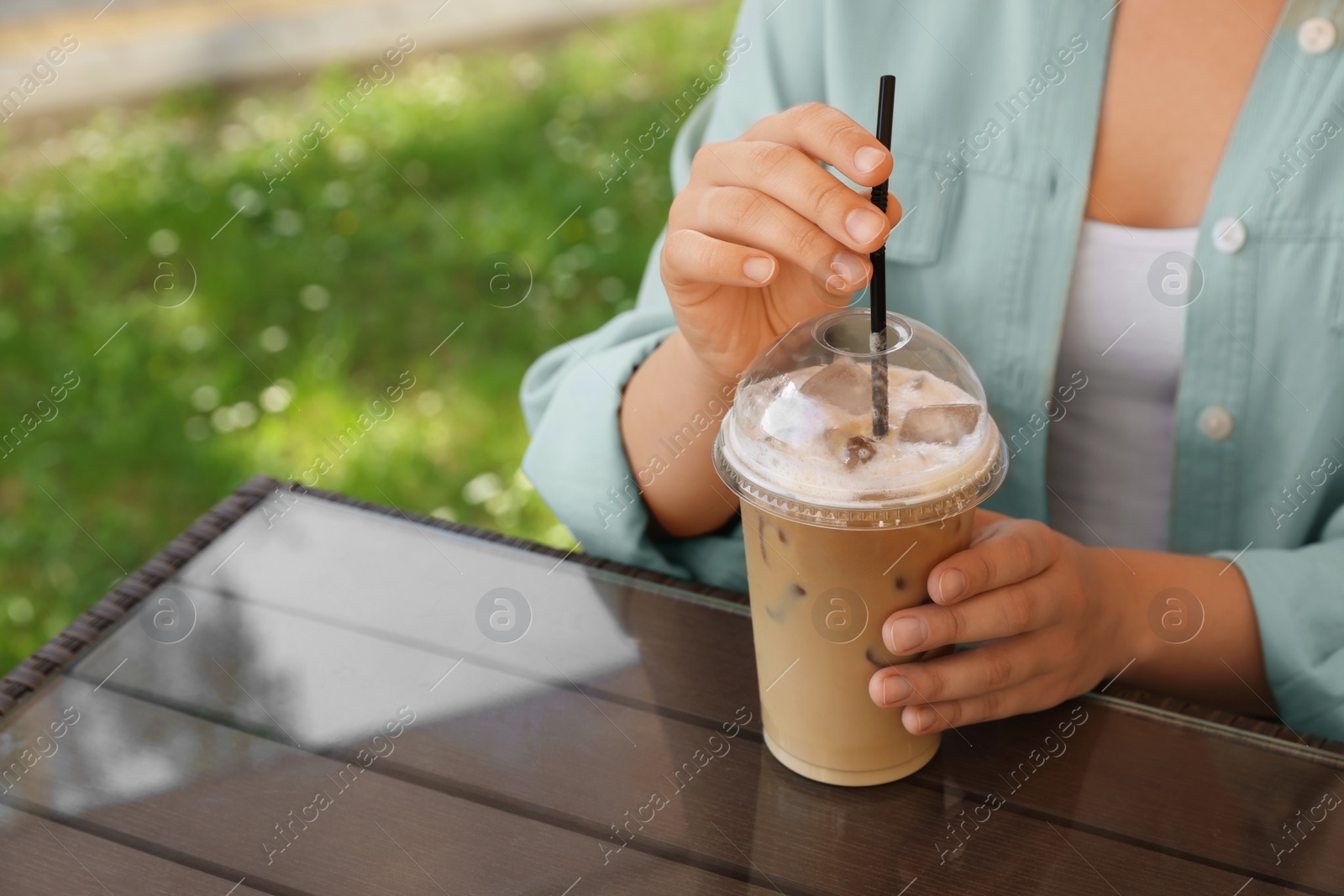 Photo of Woman with plastic takeaway cup of delicious iced coffee at table in outdoor cafe, closeup. Space for text