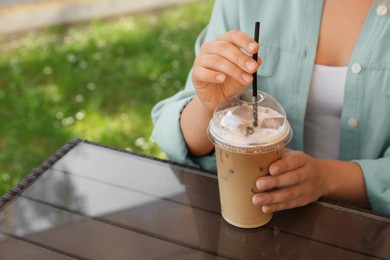 Photo of Woman with plastic takeaway cupdelicious iced coffee at table in outdoor cafe, closeup. Space for text