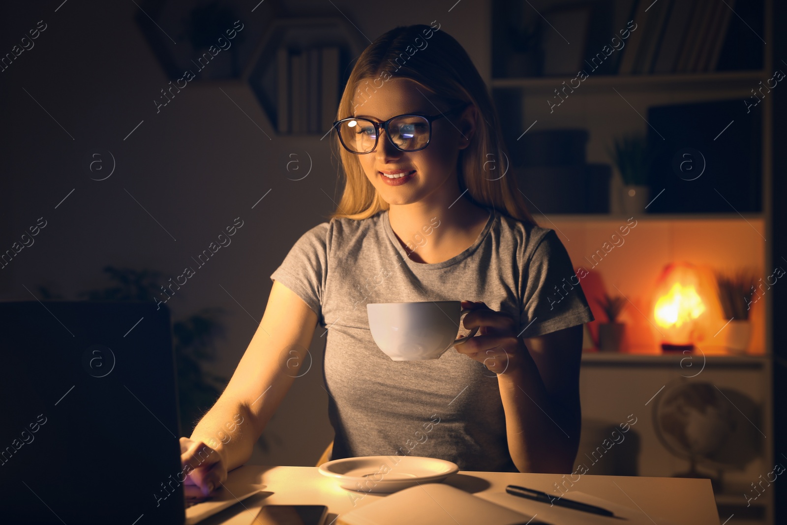 Photo of Home workplace. Woman with cup of hot drink working on laptop at white desk in room