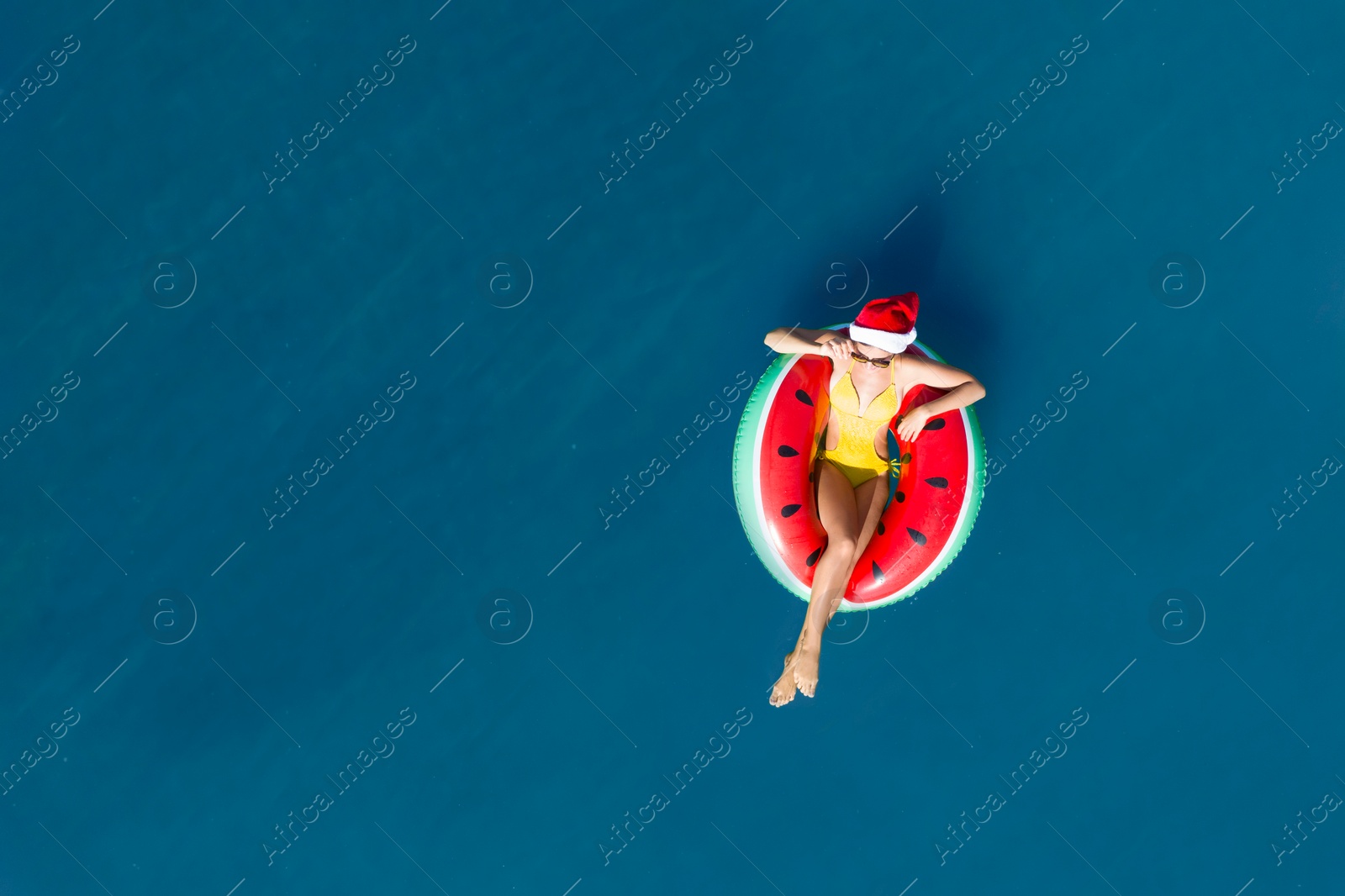 Image of Young woman wearing Santa hat and swimsuit with inflatable ring in sea, top view. Christmas vacation