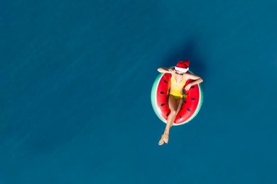 Young woman wearing Santa hat and swimsuit with inflatable ring in sea, top view. Christmas vacation