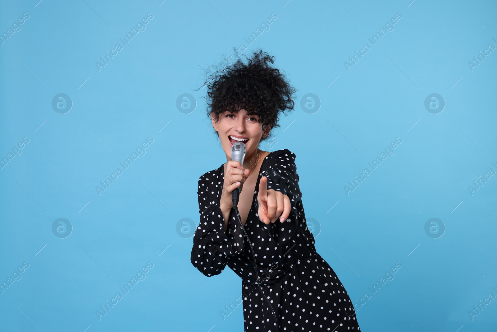 Photo of Beautiful young woman with microphone singing on light blue background