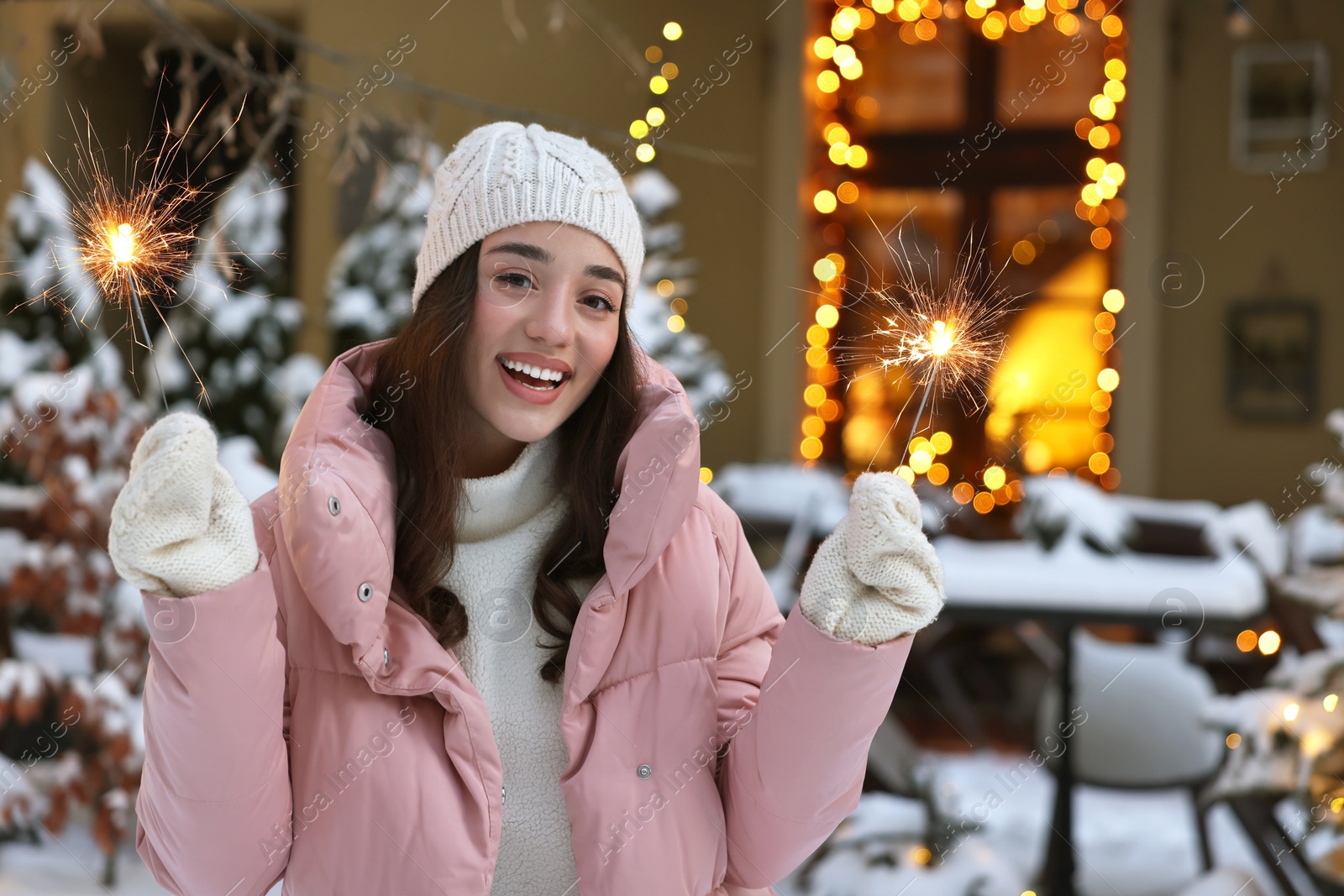 Photo of Portrait of happy woman with burning sparkles on snowy city street. Space for text