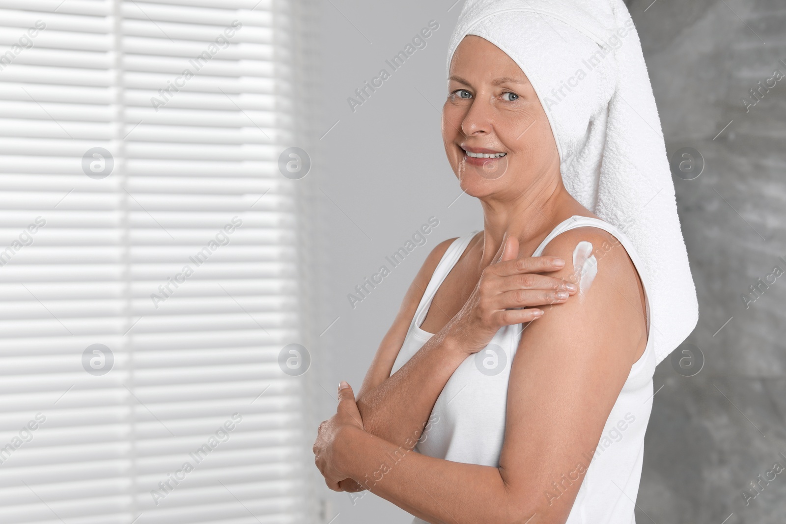 Photo of Happy woman applying body cream onto shoulder indoors. Space for text