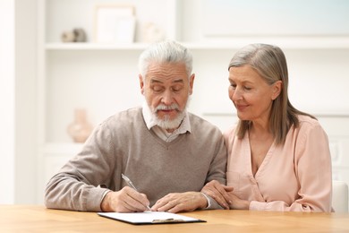 Senior couple signing Last Will and Testament indoors