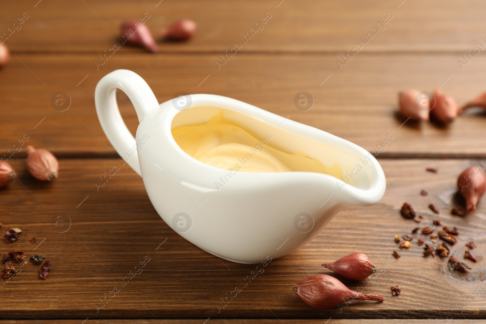 Photo of Tasty sauce in gravy boat, small onion bulbs and spice on wooden table