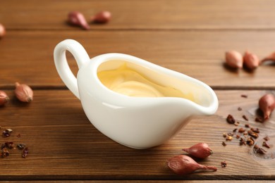 Photo of Tasty sauce in gravy boat, small onion bulbs and spice on wooden table