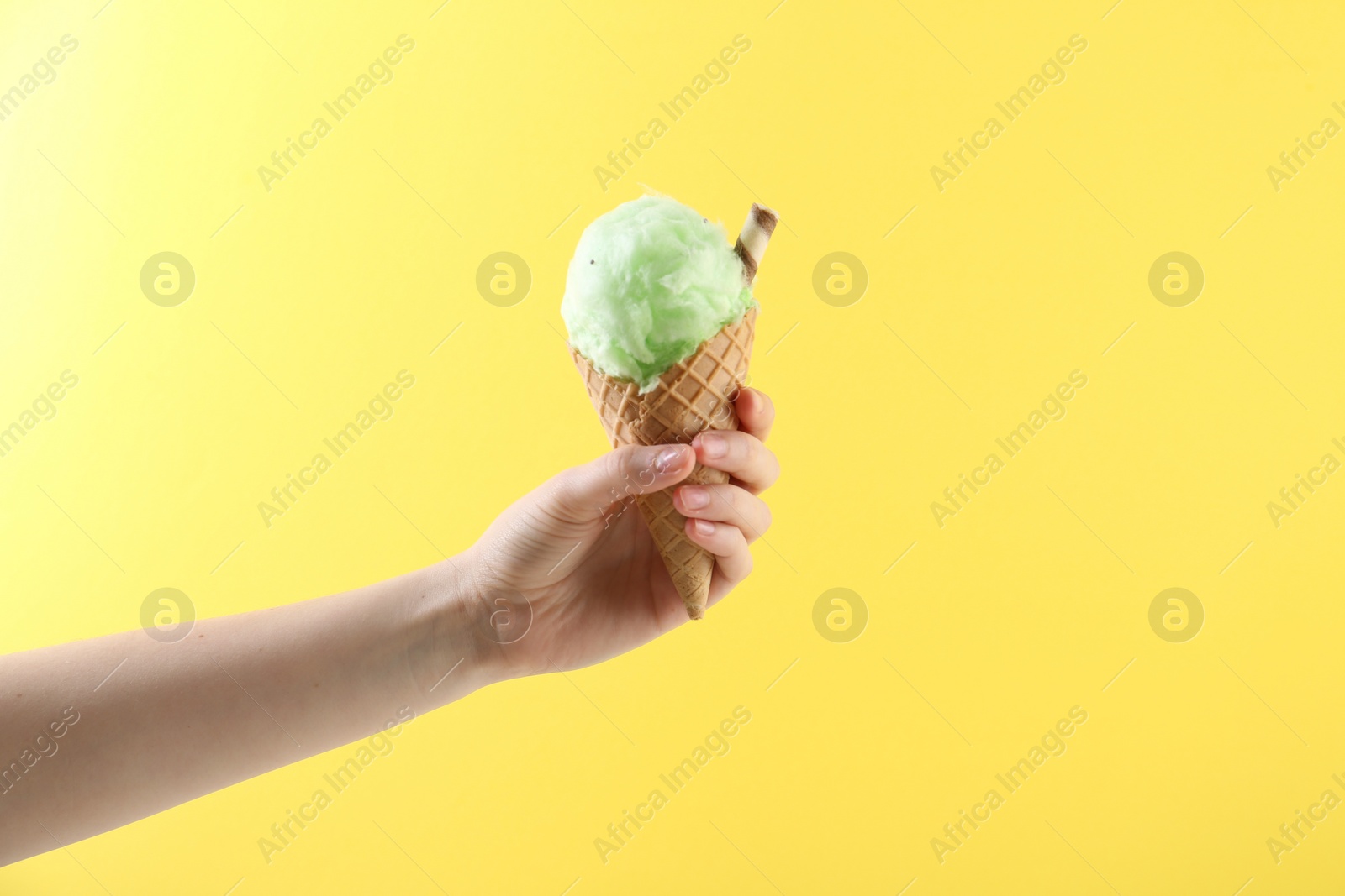 Photo of Woman holding waffle cone with cotton candy on yellow background, closeup