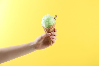 Woman holding waffle cone with cotton candy on yellow background, closeup