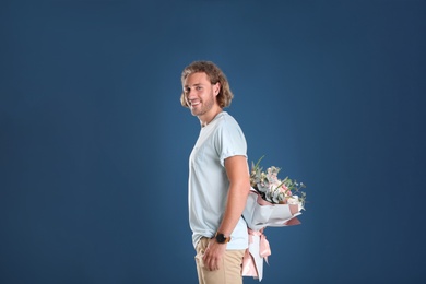Photo of Young handsome man hiding beautiful flower bouquet behind his back on blue background