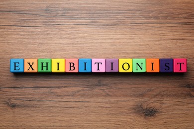 Photo of Word EXHIBITIONIST made with colorful cubes on wooden table, flat lay
