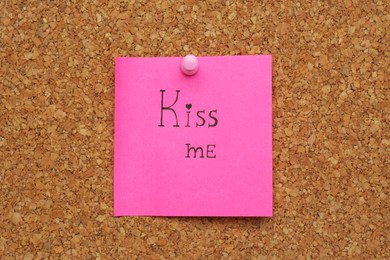 Photo of Pink paper note with phrase Kiss Me pinned to cork board