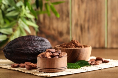 Photo of Bowl of cocoa beans, pod and powder on table, space for text