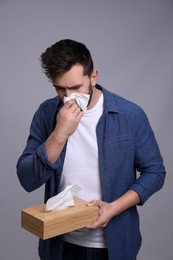 Photo of Man sneezing on grey background. Cold symptoms