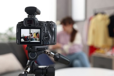 Photo of Fashion blogger explaining something while recording video at home, focus on camera