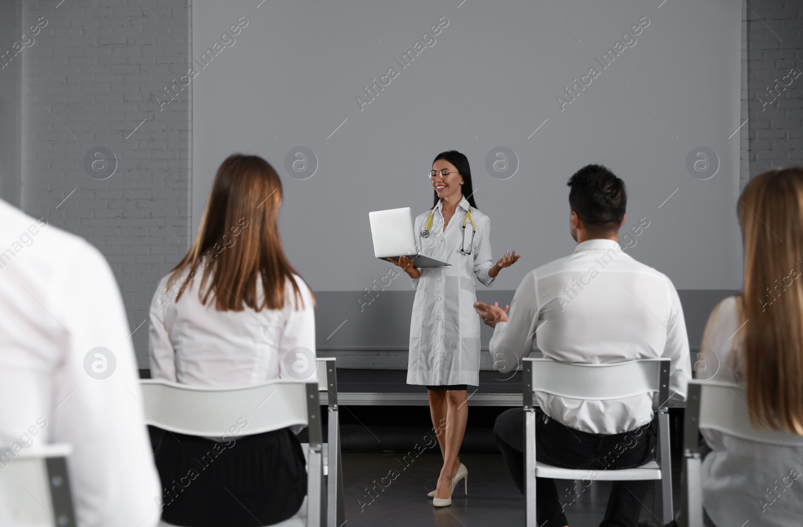 Photo of Female doctor with laptop giving lecture in conference room with projection screen