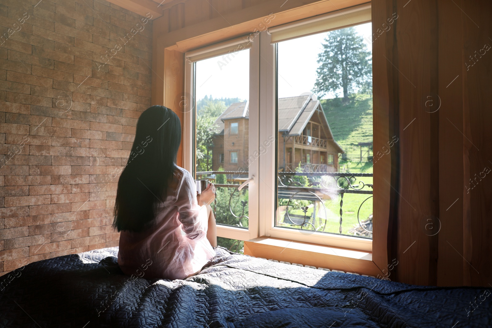 Photo of Young woman sitting on bed and enjoying view from window. Peaceful morning