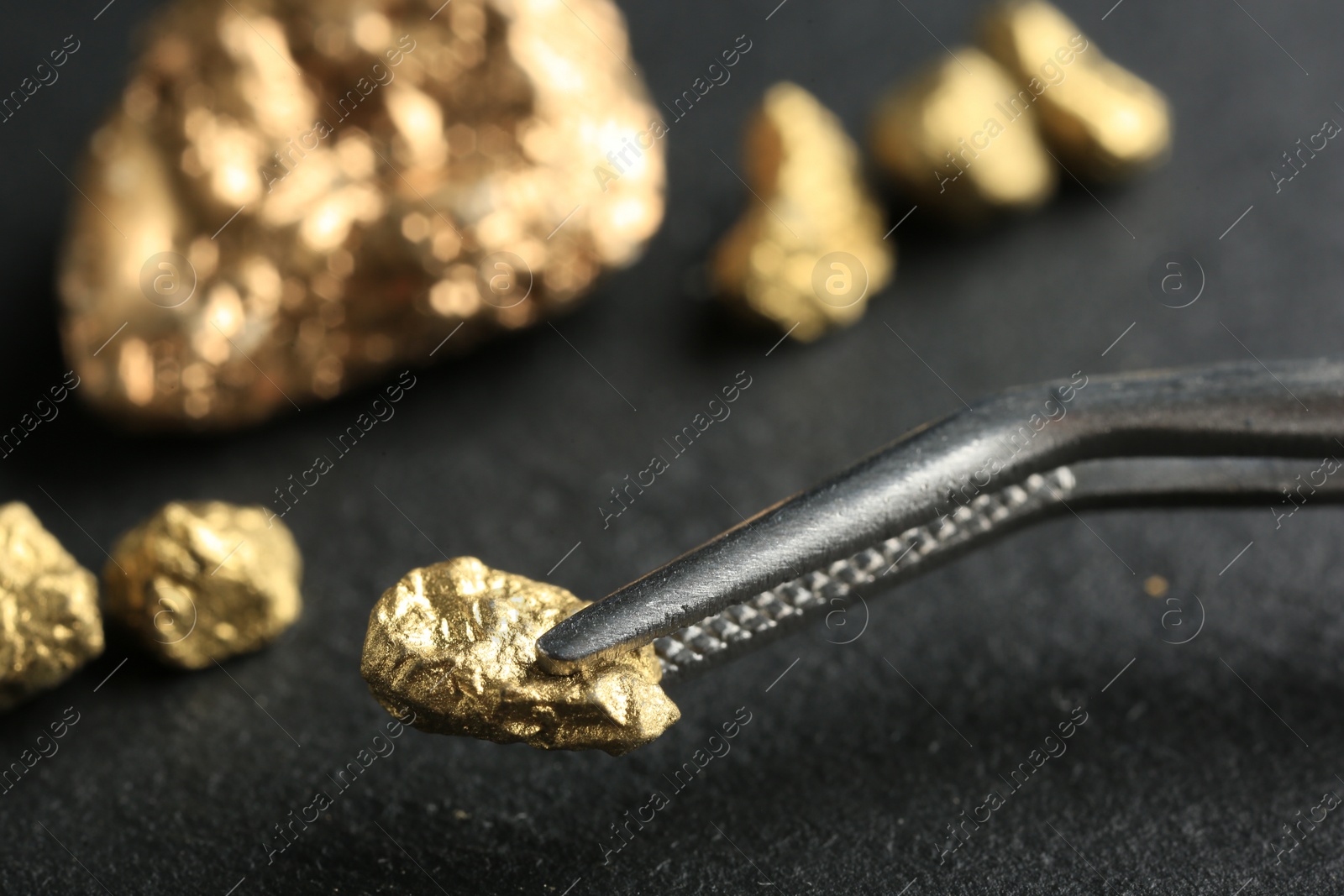 Photo of Tweezer with shiny gold nugget over grey surface, closeup