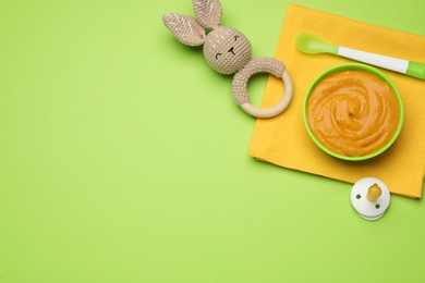 Photo of Toy, pacifier and plastic dishware with healthy baby food on light green background, flat lay. Space for text