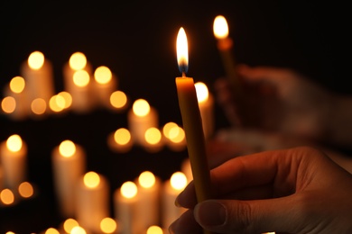 Woman holding burning candle in darkness against blurred background, closeup. Space for text
