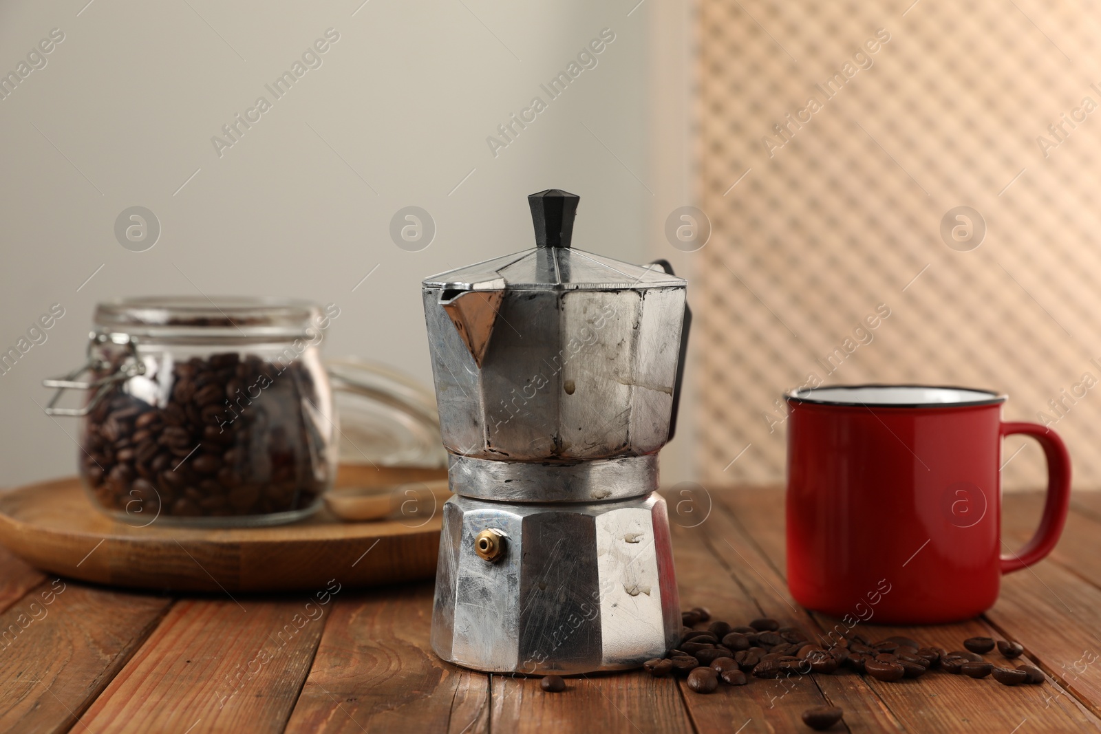 Photo of Moka pot, coffee beans and red mug on wooden table indoors
