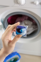 Woman holding laundry detergent capsule near washing machine, closeup