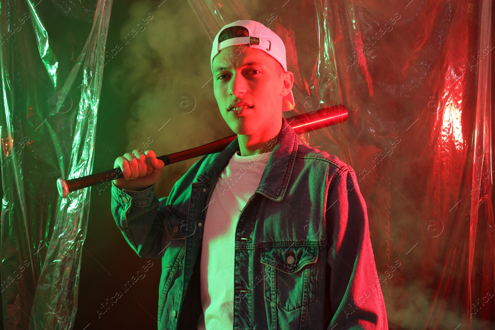 Photo of Young man with baseball bat on color background in neon lights