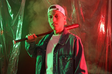 Photo of Young man with baseball bat on color background in neon lights