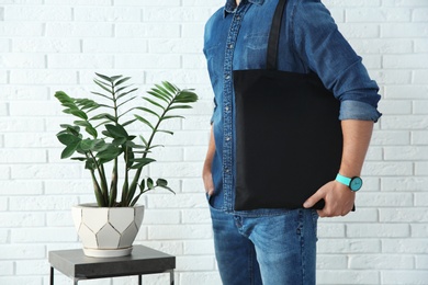 Young man holding textile bag against brick wall, closeup.  Mockup for design