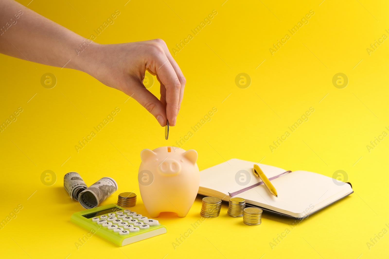 Photo of Financial savings. Woman putting coin into piggy bank on yellow background, closeup