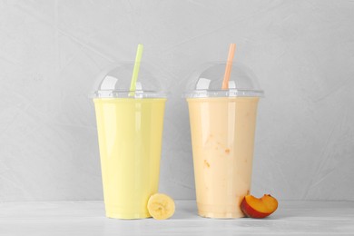 Plastic cups of different tasty smoothie and fresh fruits on white wooden table