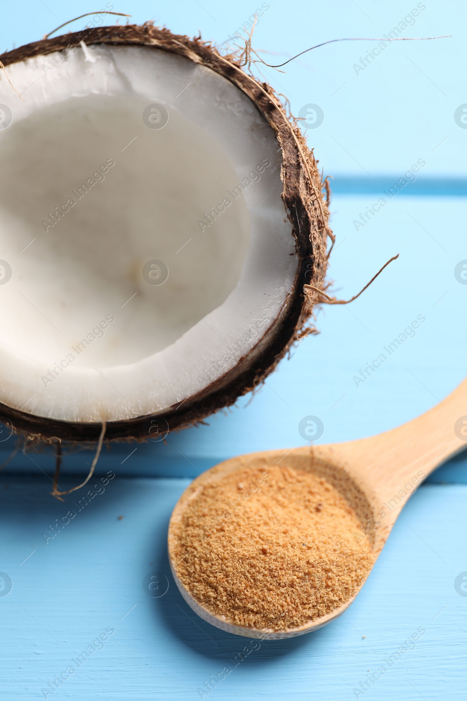 Photo of Spoon with coconut sugar and half of fruit on light blue wooden table, closeup