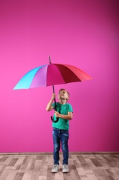 Little boy with rainbow umbrella near color wall