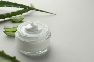 Photo of Jar with cream and cut aloe leaves on light grey background, closeup. Space for text