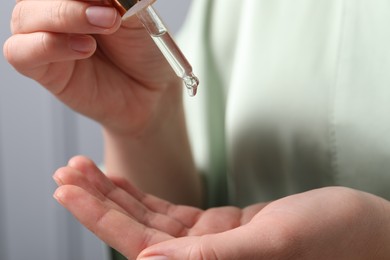 Photo of Woman applying cosmetic serum onto hand on blurred background, closeup