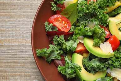 Photo of Tasty fresh kale salad on wooden table, top view