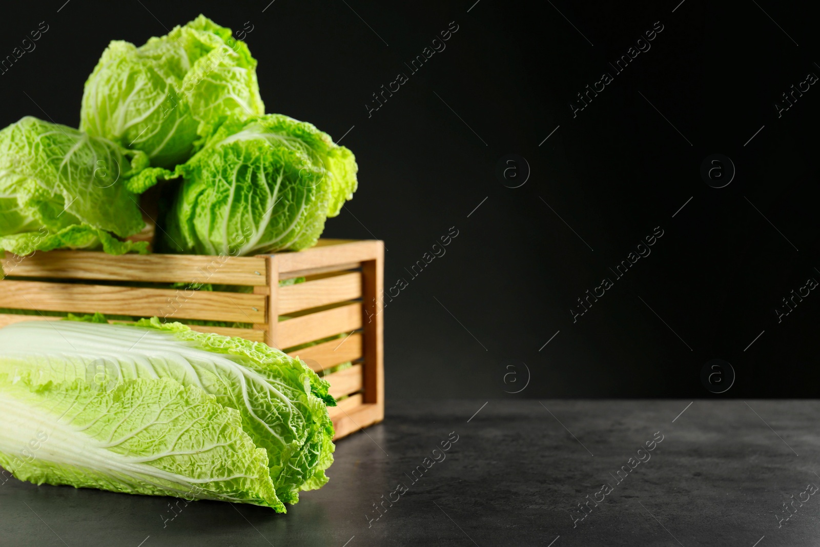 Photo of Fresh ripe Chinese cabbages and wooden crate on grey table, space for text