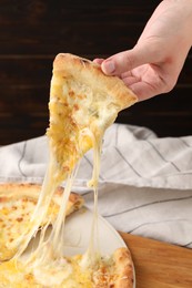 Photo of Woman taking piece of delicious cheese pizza at table, closeup