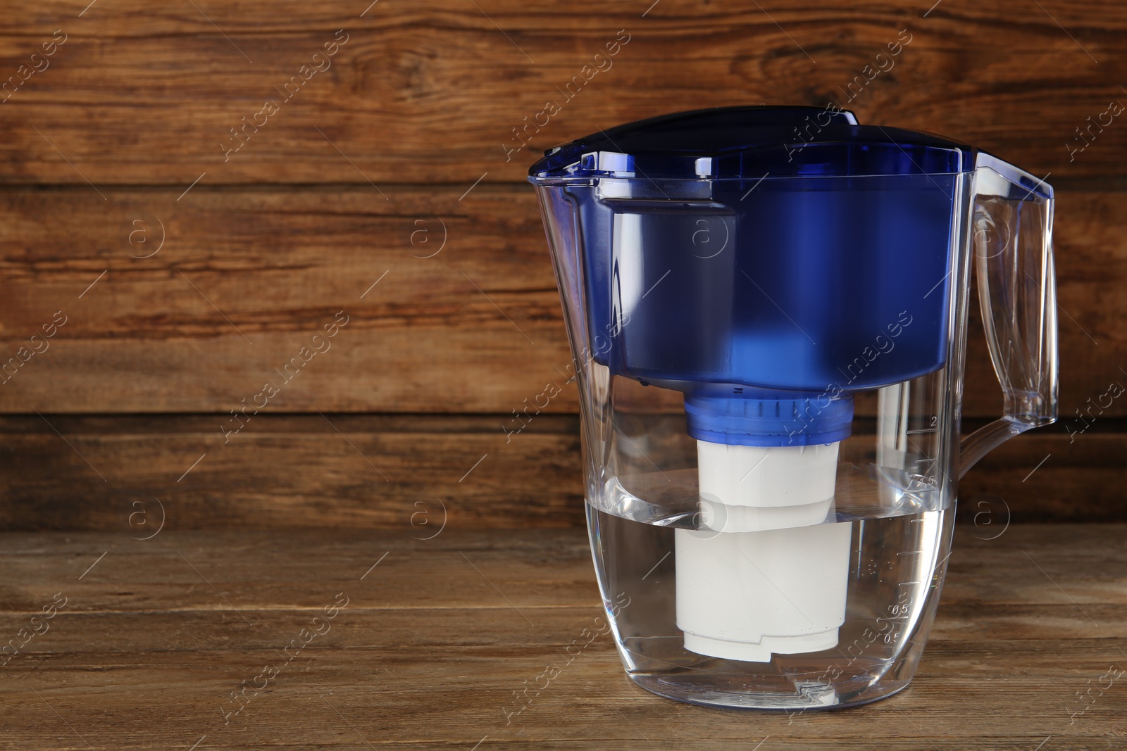 Photo of Filter jug with purified water on wooden table. Space for text