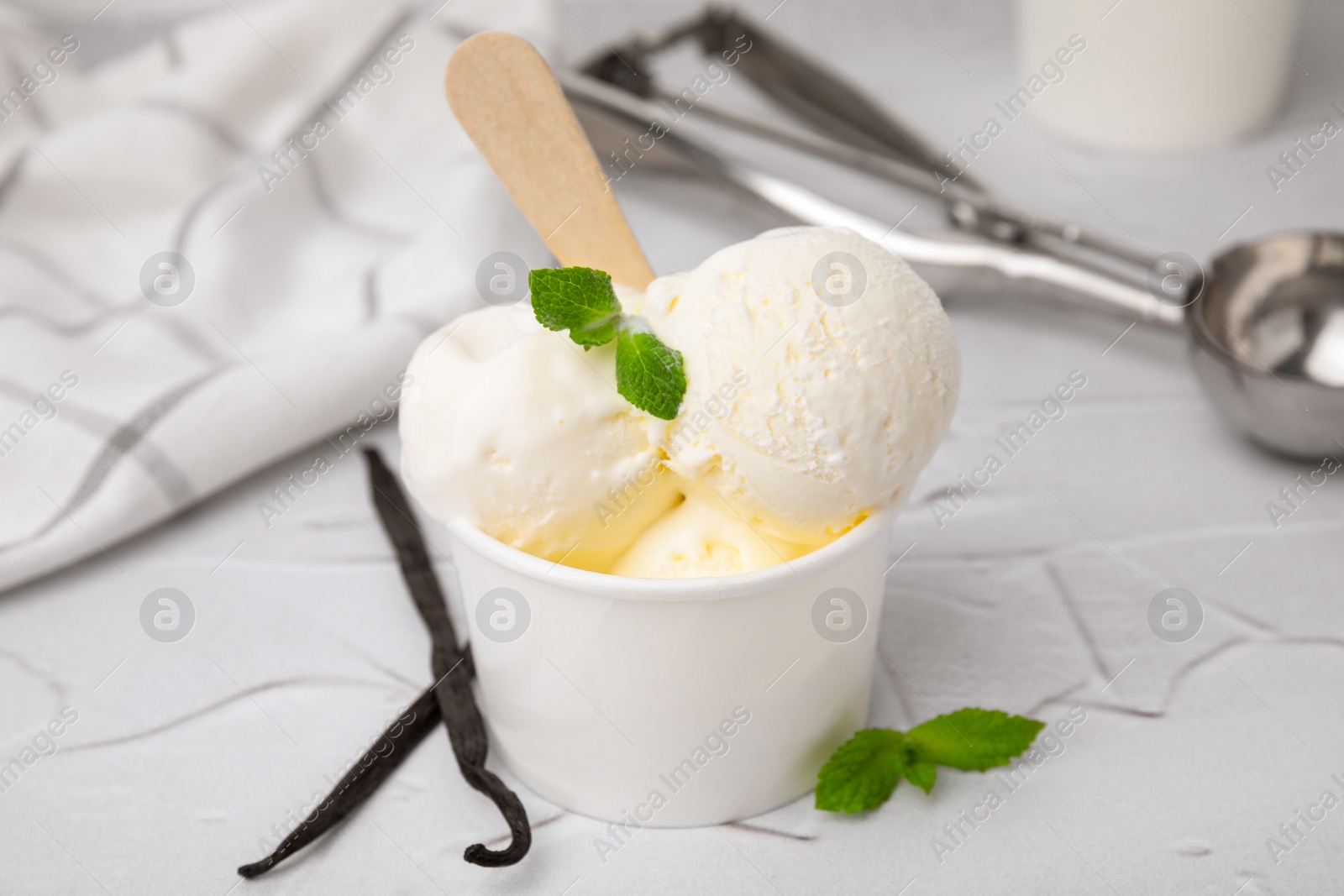 Photo of Delicious ice cream with mint and vanilla pods on white textured table, closeup