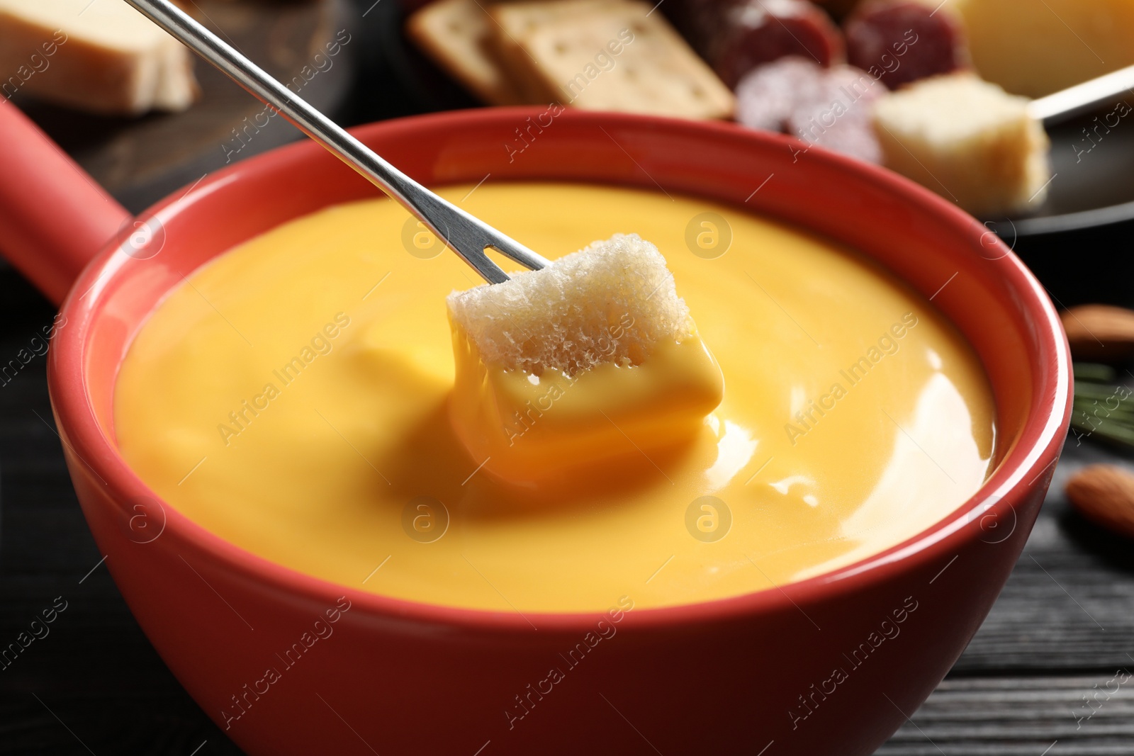 Photo of Dipping piece of bread into tasty cheese fondue at black table, closeup