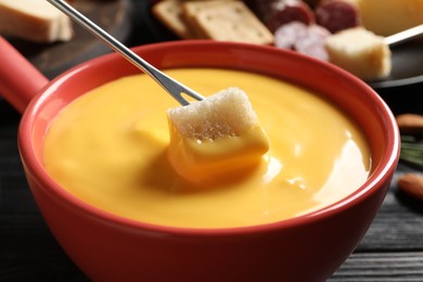 Photo of Dipping piece of bread into tasty cheese fondue at black table, closeup